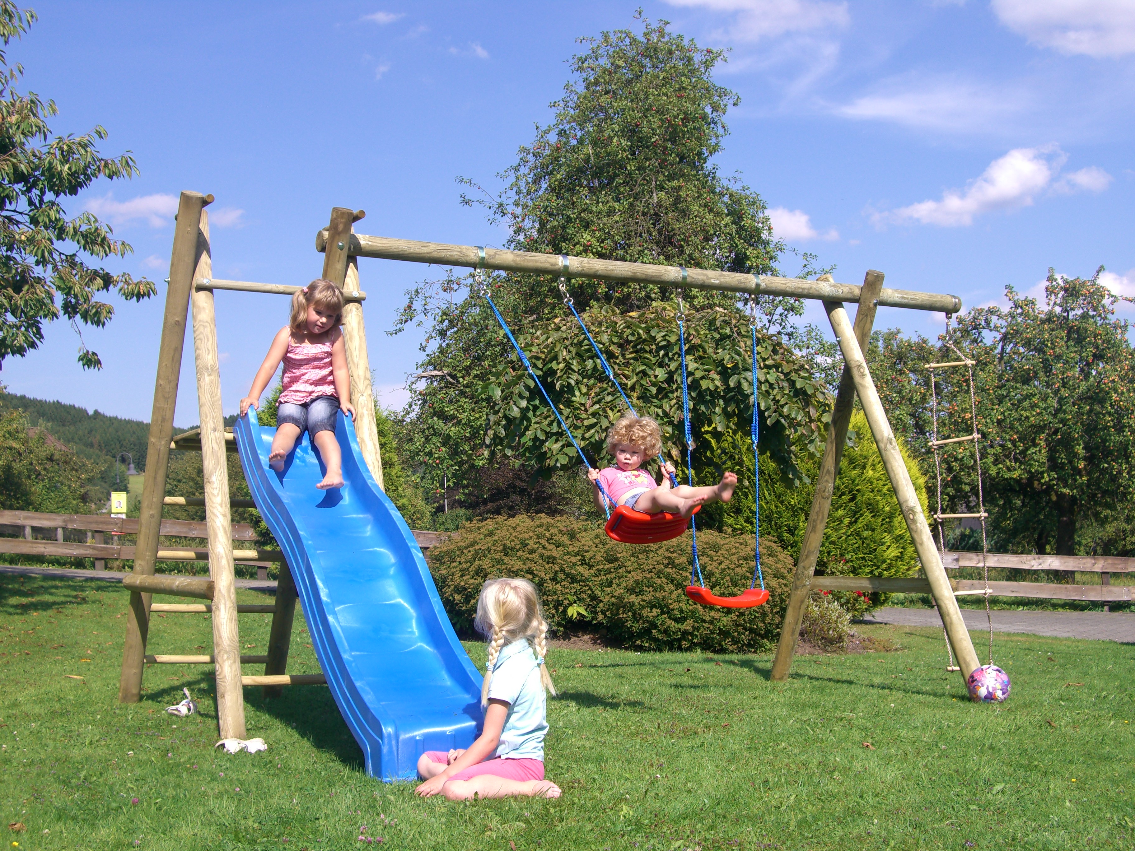 Spielanlage Drei Mädchen spielen auf einer Spielanlage mit Schaukeln und blauer Rutsche